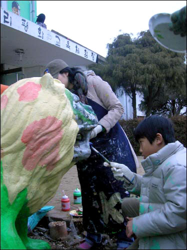 현관 앞을 지키고 있는 무서운 사자상도 고운 옷을 입었다. 2층 벽 그림은 대추리의 소년 가수 일곱살 방병철의 얼굴. 